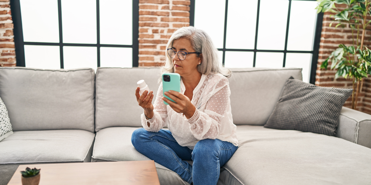 Middle age woman using smartphone holding pills at home